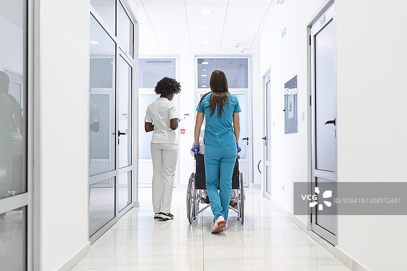 轮椅病人与专业的非洲裔美国女医生和护士专家在医院康复中心走廊图片素材