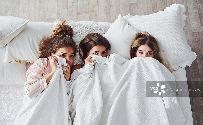 躲在毯子下面。快乐的女性朋友在卧室睡衣派对上玩得很开心图片素材