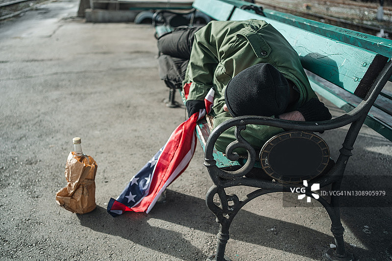 一个拿着美国国旗睡在长凳上的流浪汉图片素材