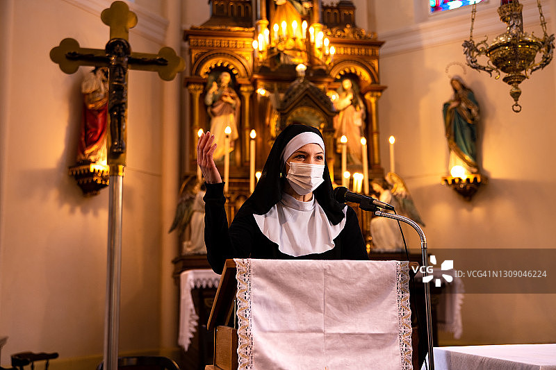 修女在罗马天主教堂读圣经，戴着防护面罩，看着人。图片素材