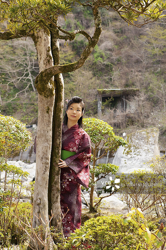 美丽的年轻女子在树在日本和服在宁静的公园图片素材