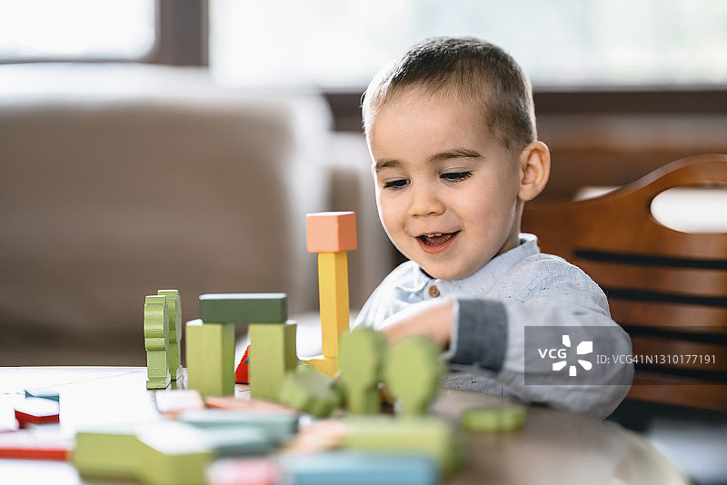 快乐的蹒跚学步的小男孩在家里玩五颜六色的玩具积木图片素材