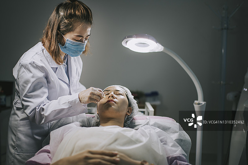 美容师在手术开始前用棉球清洗亚洲华人妇女的脸，在手术室等待治疗图片素材
