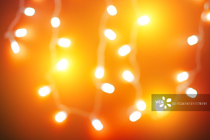 散焦明亮的圣诞节背景与发光的散焦彩色花环灯在红色照明闪烁。新年庆祝概念图片素材