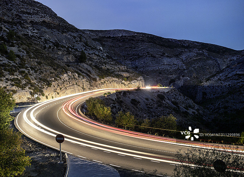 高角度视角的移动汽车和卡车灯循环沿着道路的山与圆形曲线关闭在夜晚。图片素材
