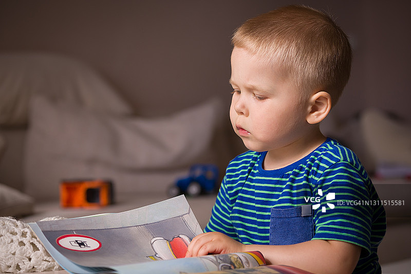 一个穿着条纹t恤的小男孩在儿童游戏室里看书。教育与知识观念。儿童阅读。为上学做准备。享受阅读。图片素材