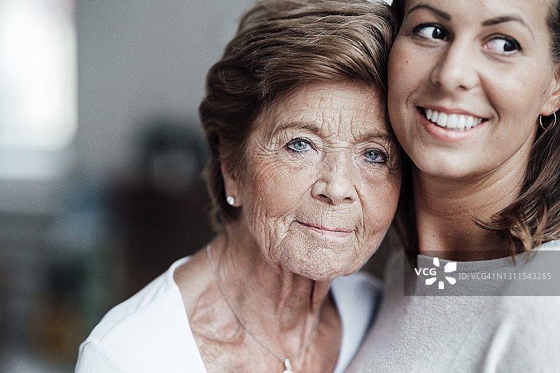 蓝眼睛的老妇人在家里拥抱微笑的孙女图片素材
