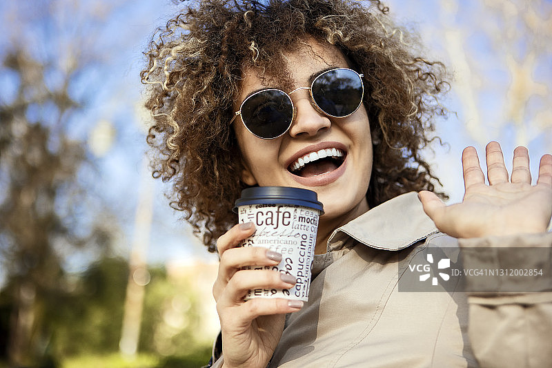 微笑的年轻女子挥手，喝着外卖咖啡图片素材