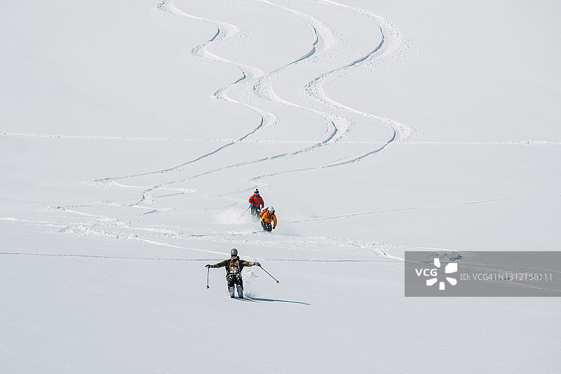 三个滑雪者一起滑下满是粉末的山坡图片素材