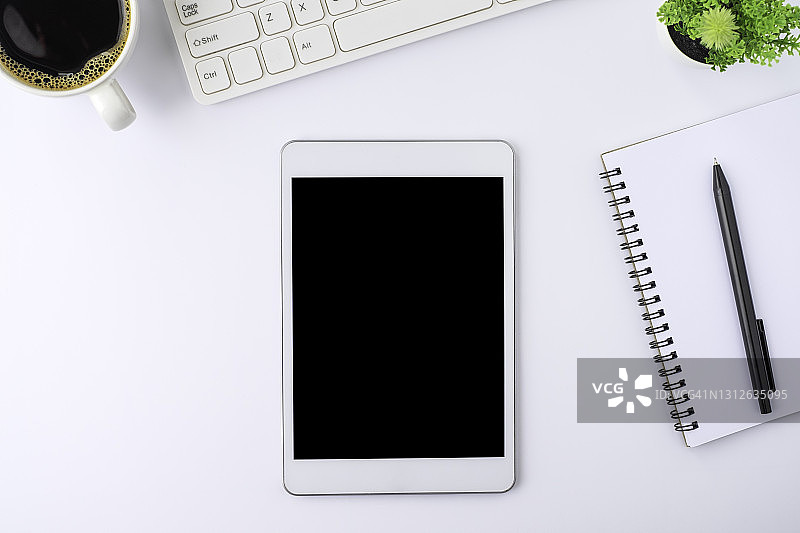 俯视图上方的平板电脑空白显示器黑屏上的白色办公桌桌子上有笔记本，键盘，咖啡杯。工作空间，办公业务技术。教育与经营理念。平躺图片素材