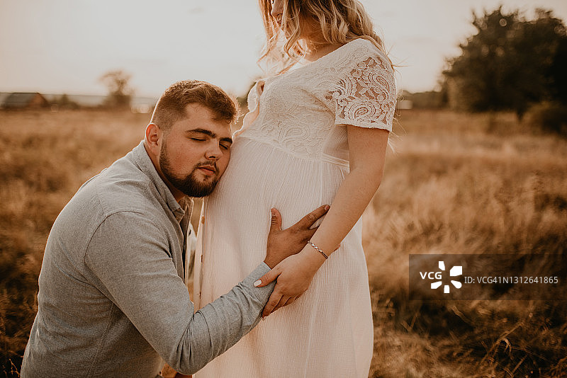 丈夫抱着怀孕的妻子，爸爸听着肚子把耳朵贴在肚子上图片素材