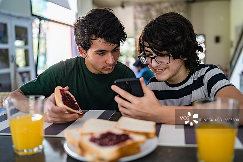 青少年一边吃早餐一边玩手机图片素材