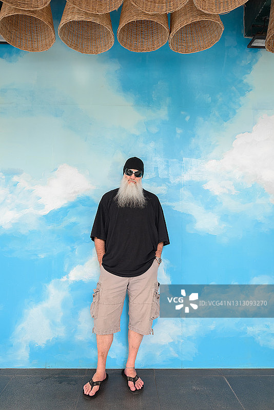 长胡子的成熟男子站在户外的蓝天和云背景墙的全长镜头图片素材