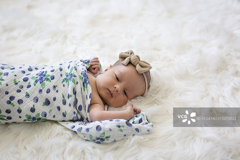 一个刚出生的女婴被裹在毯子里，躺在松软的白色地毯上图片素材