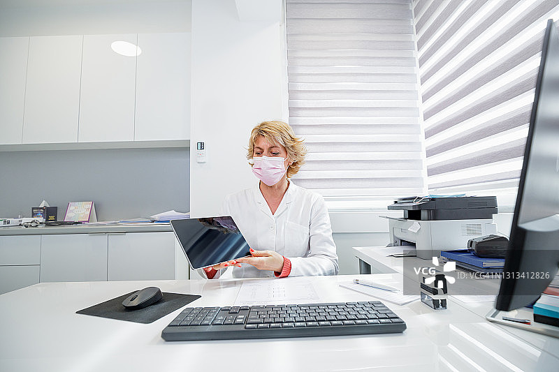 女医生戴着保护面罩，在她的办公桌前拿着数字平板电脑图片素材