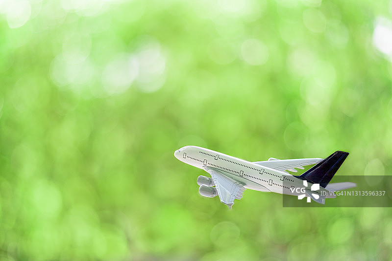 白色的商用飞机/飞机飞过绿色的散焦背景图片素材