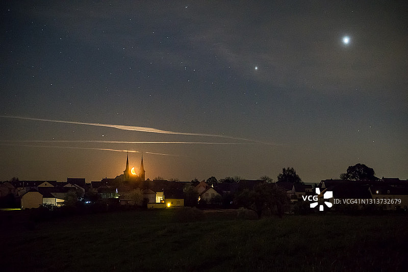 新月升起在两座教堂之间的德国村庄与火星，木星和土星图片素材