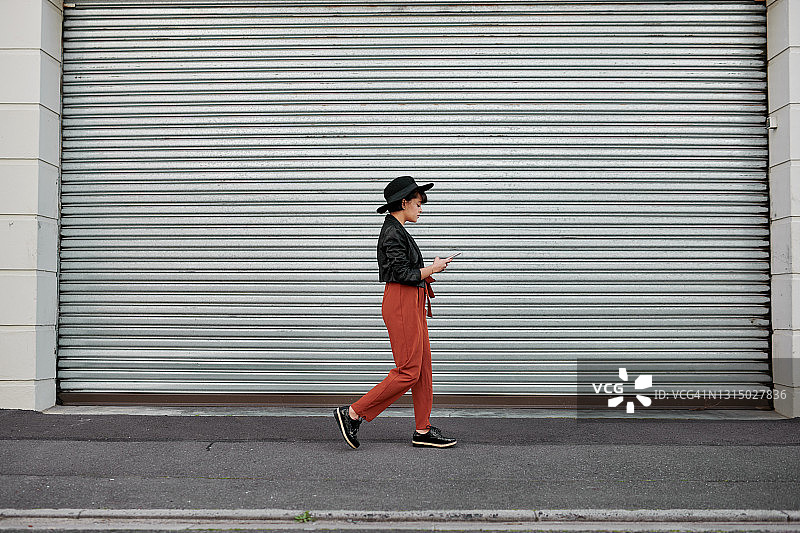 这张照片拍摄的是一位时尚的年轻女子在城市中行走时使用手机图片素材