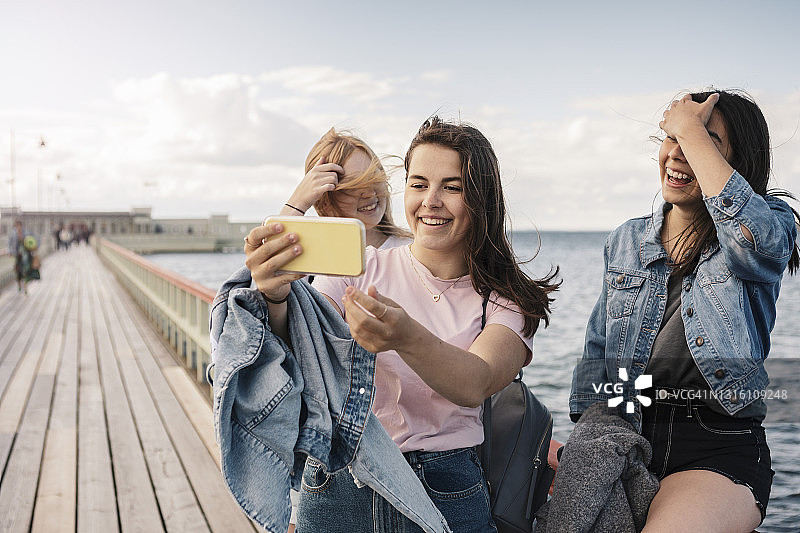 海边的码头上，快乐的女性朋友们用智能手机自拍图片素材