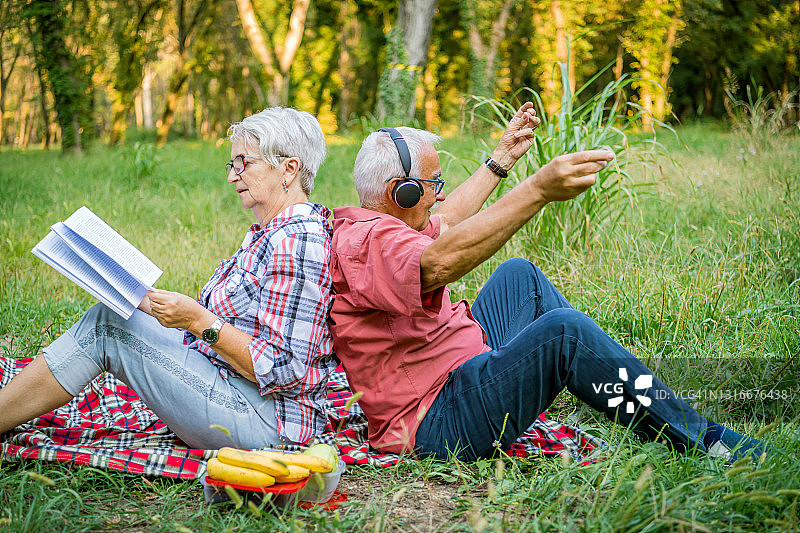 一对很棒的老夫妇正在公园里休息，一边看书，一边听音乐图片素材