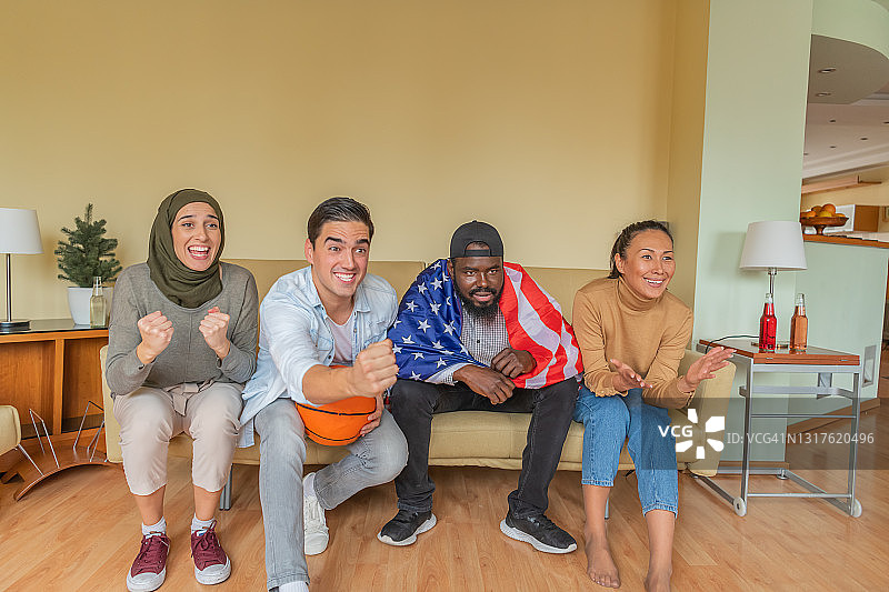 来自美国的兴奋的多文化朋友正在家里享受一场篮球赛。图片素材