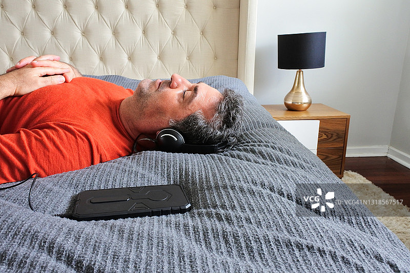 一个成年人在床上听音乐的侧视图图片素材