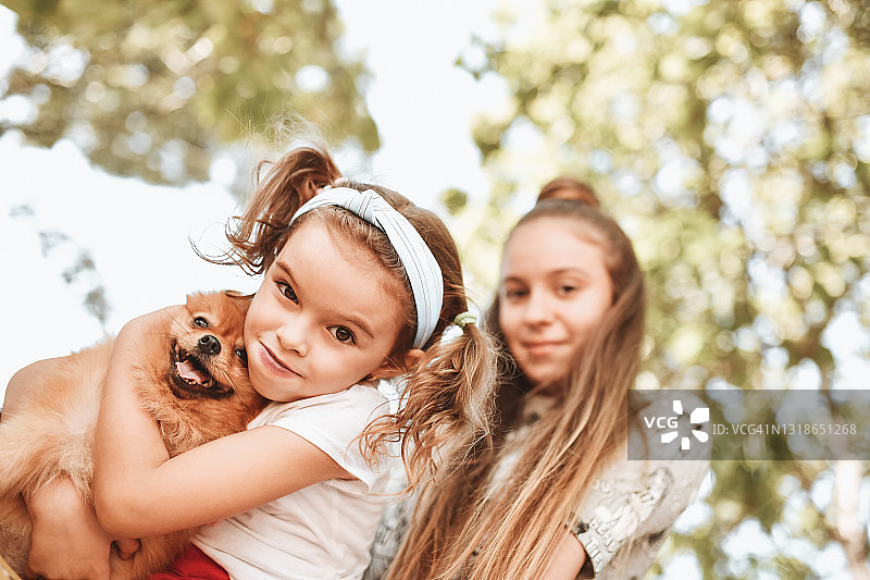 可爱的小女孩和十几岁的妹妹在外面玩博美犬图片素材