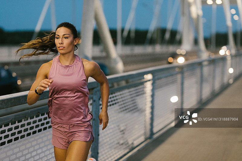 女运动员黄昏时在桥上跑步图片素材