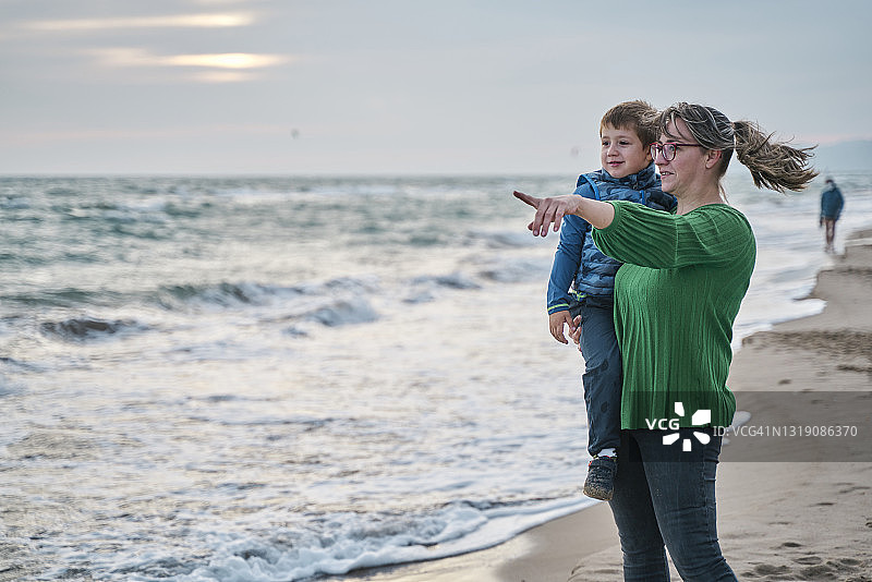 妈妈抱着她的小男孩，在海滩上微笑着图片素材