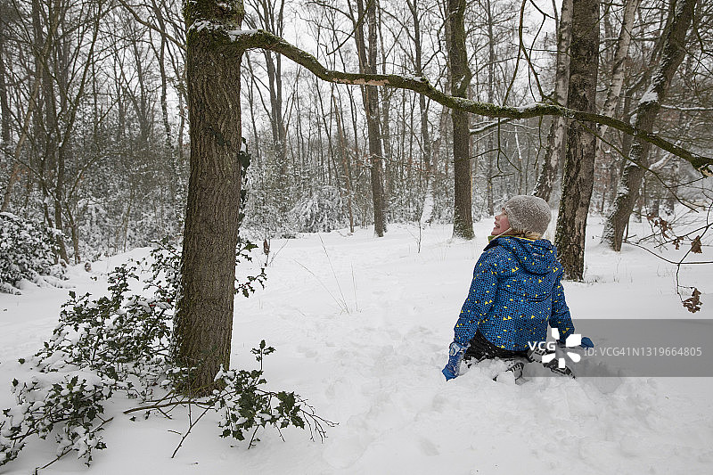 冬天跪在树旁的雪地上，男孩看向别处图片素材