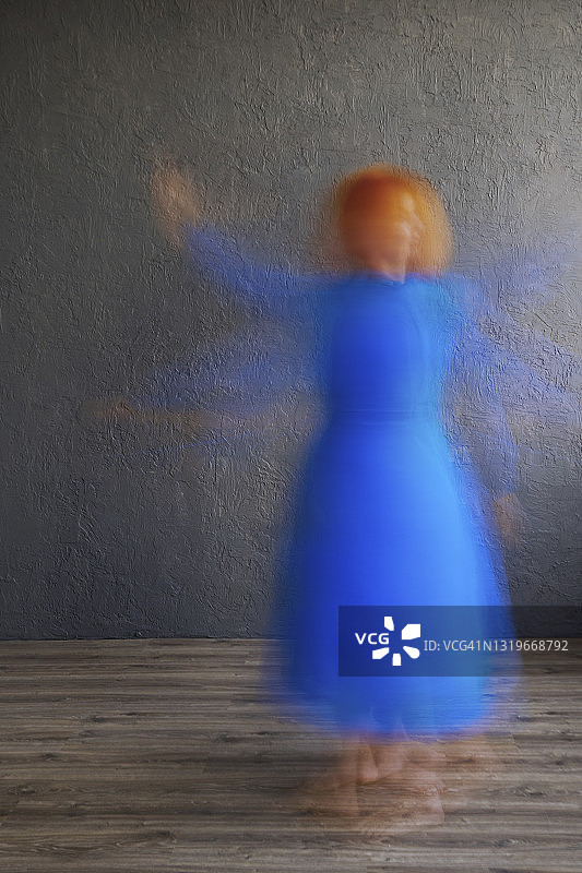 穿着蓝色裙子的女人在灰色的墙前跳舞图片素材