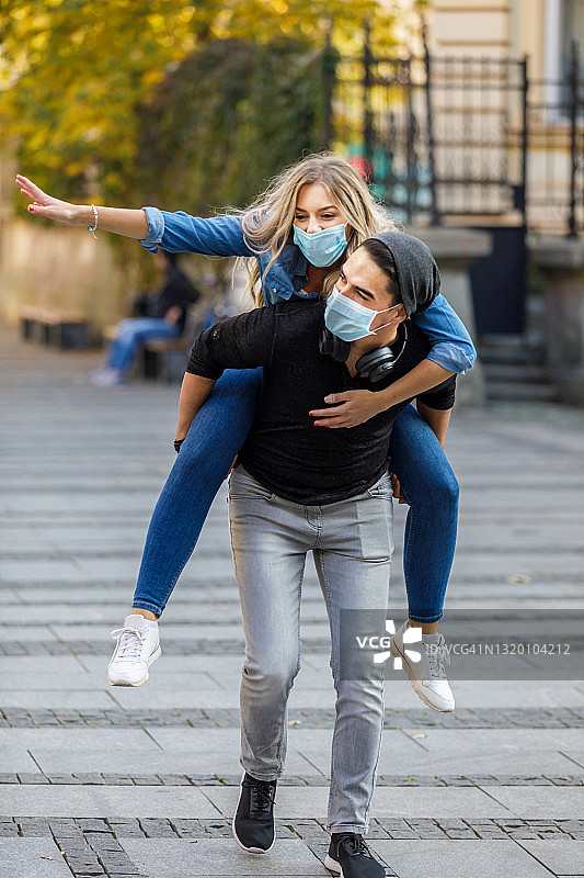 一对快乐的年轻情侣戴着面具在城市街道上拥抱，玩得很开心。图片素材