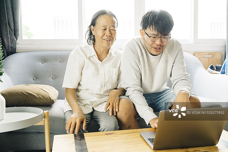 亚洲年轻成人儿子教他的老母使用笔记本电脑进行视频通话和在家里使用社交媒体图片素材