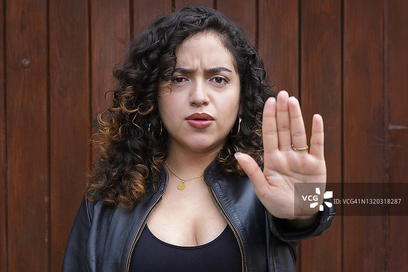 一位年轻的拉丁美洲女性，一头卷发，看着镜头，示意停止图片素材