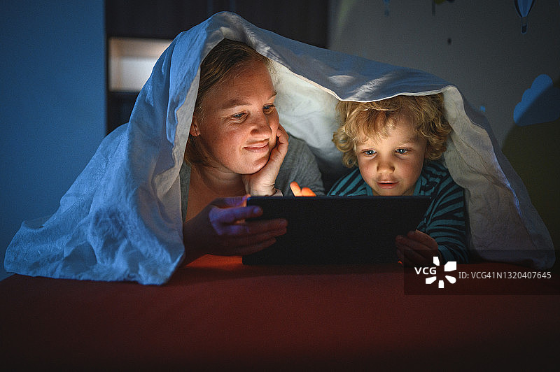可爱的金发男孩和他的妈妈在睡觉时使用电子平板电脑图片素材