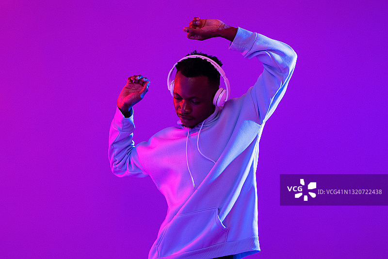 年轻英俊的非洲男子戴着耳机听音乐和跳舞在未来的紫色赛博朋克霓虹灯光背景图片素材