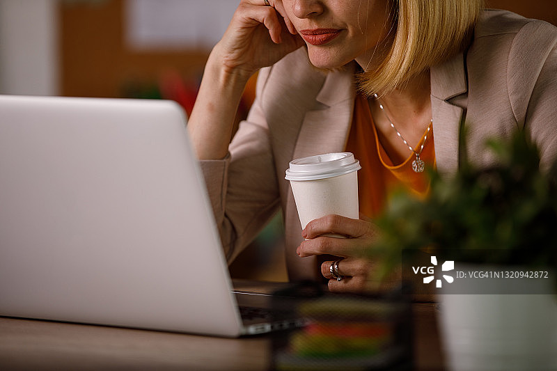 女商人一边喝着咖啡一边使用笔记本电脑图片素材