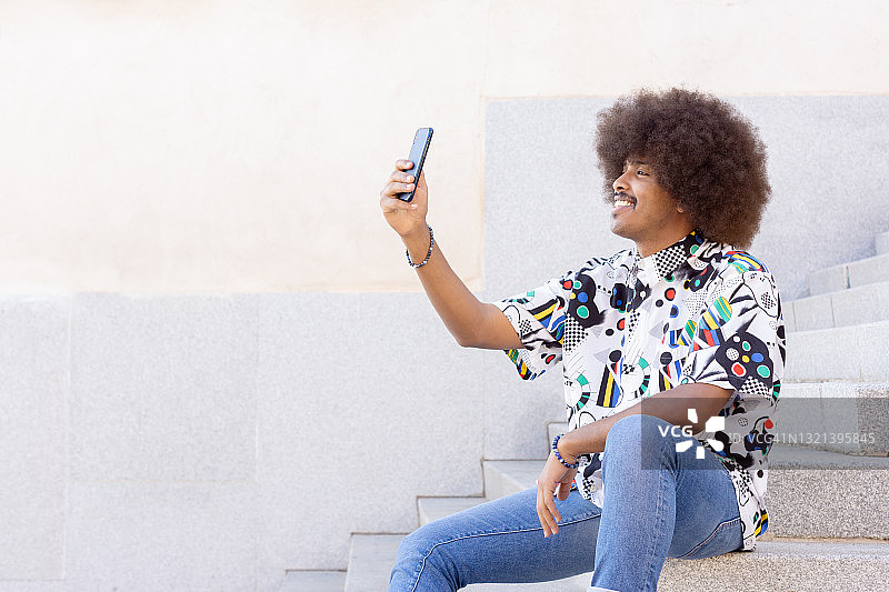 一个留着非洲式发型的黑人微笑着坐在石阶上用智能手机自拍图片素材