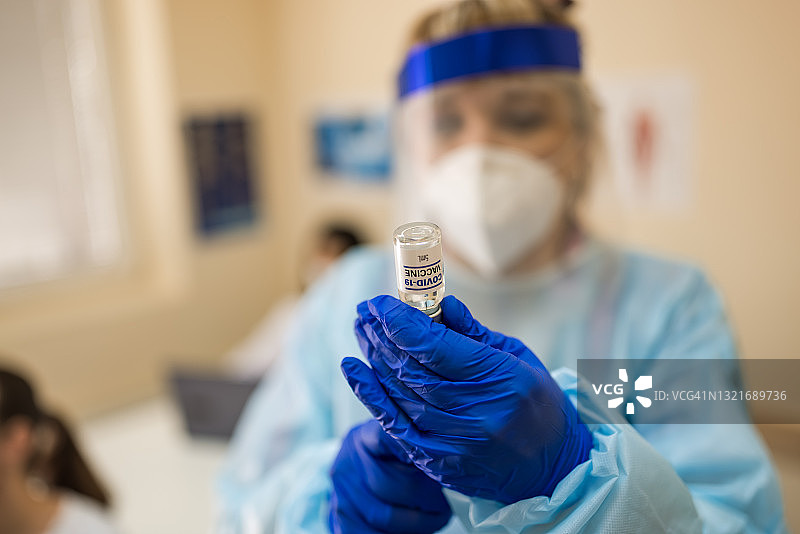 身着个人防护服的女医务人员向注射器内注入Covid-19疫苗瓶液体图片素材