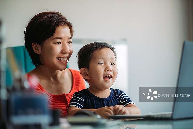 亚裔华人母亲与儿子工作和使用笔记本电脑在办公室图片素材