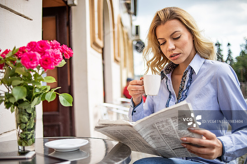 一个年轻漂亮的女人正在一家咖啡馆的花园里喝她的早晨咖啡。图片素材