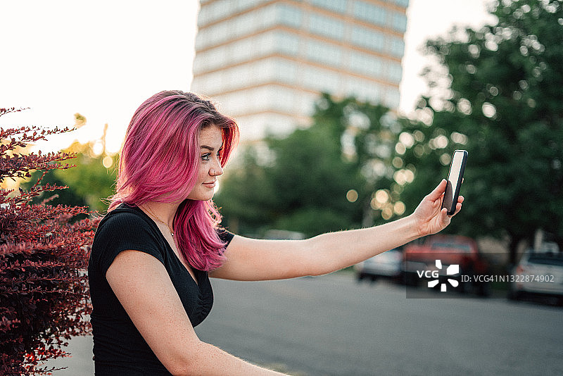 一个时尚的年轻女人的肖像与有趣的粉红色头发在户外在夏天自拍图片素材