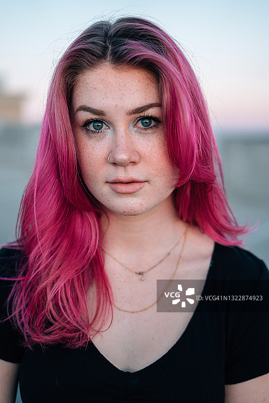 一个时尚的年轻女人的艺术肖像与有趣可爱的亮粉色染发看着相机从一个停车场的顶部在城市户外在夏天图片素材