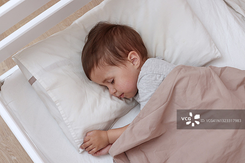 安静可爱的蹒跚学步的婴儿睡在他的床上。睡着的孩子的概念。两岁的孩子睡在家里。图片素材