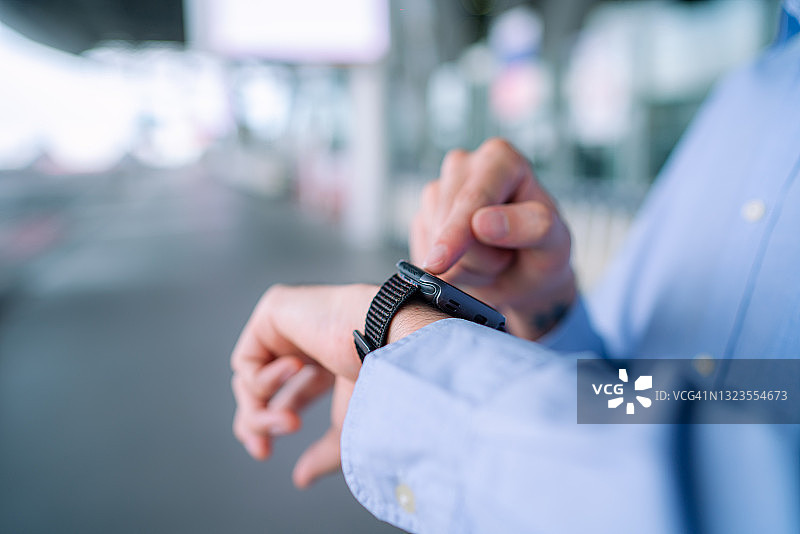 一名年轻的亚洲男子拿着旅行箱和护照走在机场大厅里，看手表上的时间图片素材
