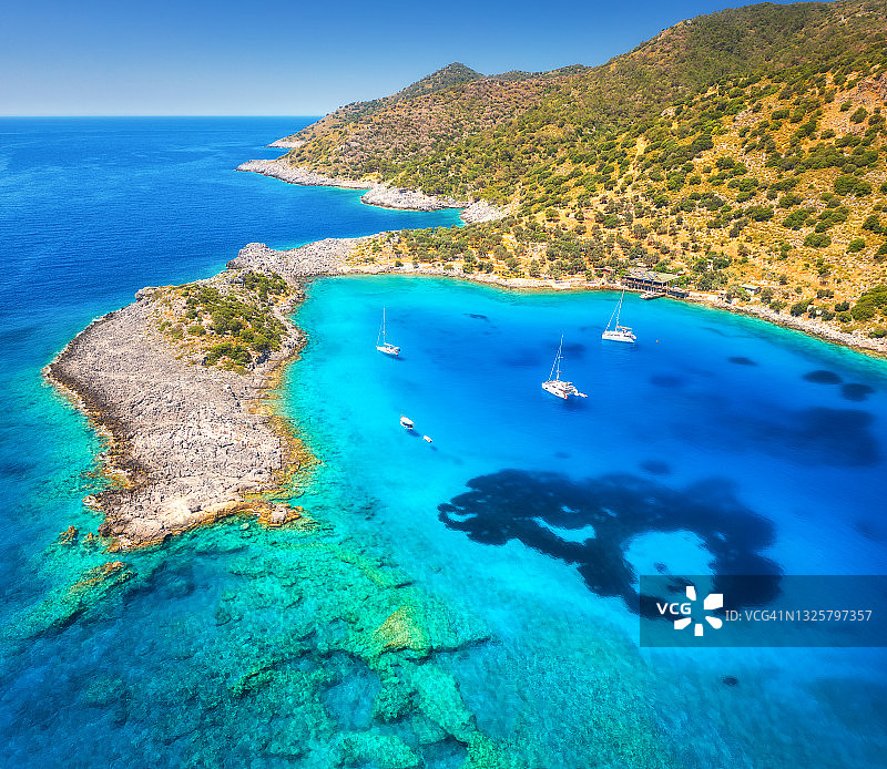夏天日落时海上美丽的游艇和船只的鸟瞰图。Akvaryum koyu在土耳其。豪华游艇，帆船，清澈的蓝色的水，岩石，天空，山和绿色的树木。旅行图片素材