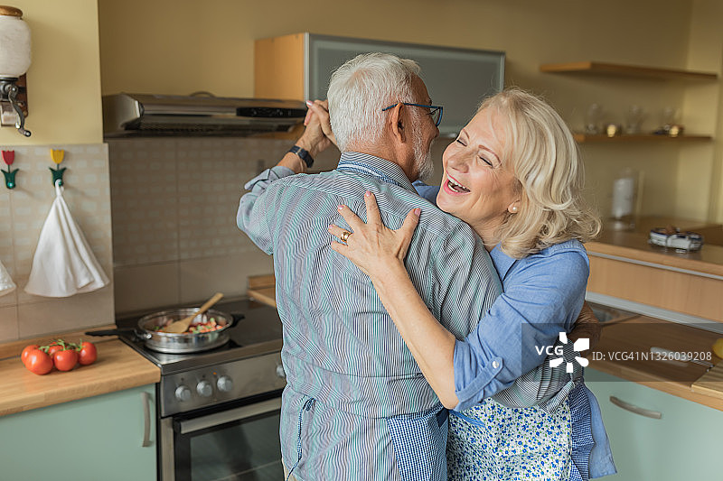 一对老年夫妇在家做饭时享受舞蹈。图片素材