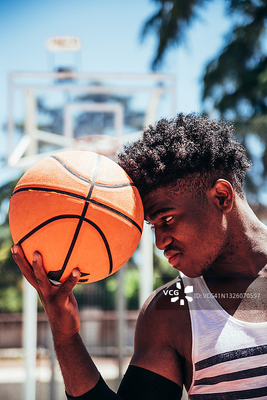 一个黑人非洲裔男孩的肖像，他的前额拿着一个篮球在城市篮球场上。图片素材