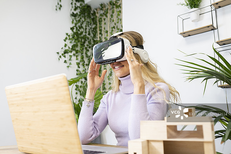 金发碧眼的女商人戴着虚拟现实模拟器坐在办公室的办公桌前图片素材