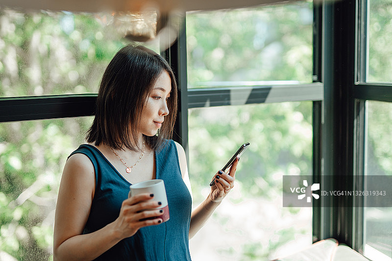 年轻女子边喝咖啡边用智能手机图片素材